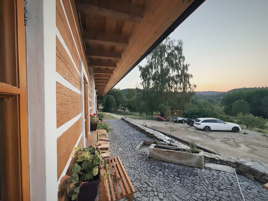Dlážděná cesta podél roubené stěny, za ní louka a západ slunce
